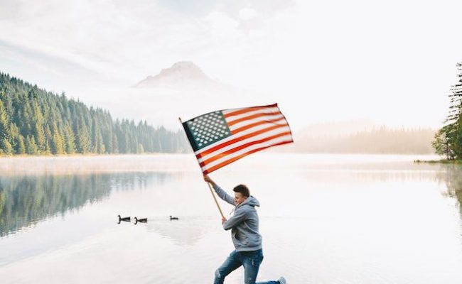 Person Leaping On Lake Rocks With American Flag